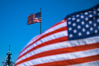 Low angle view of flags waving against clear blue sky