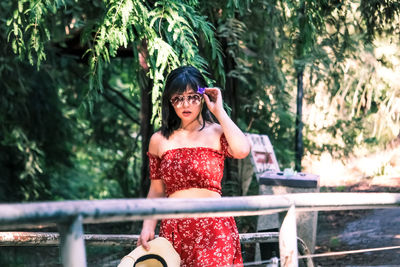 Portrait of young woman standing against trees