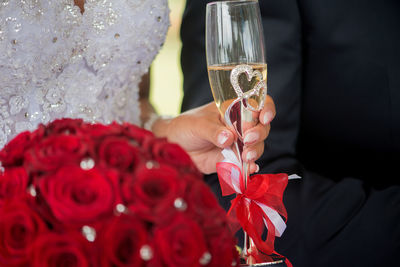 Midsection of bride holding champagne flute and red roses during wedding