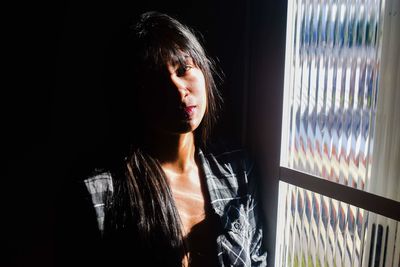 Portrait of young woman standing by window at home