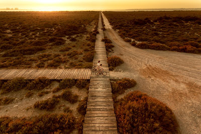 High angle view of friends riding bicycle on boardwalk during sunset