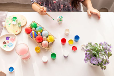 Hands of a little girl, with a brush, on a white table with multi-colored eggs in a tray