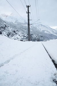 Snow covered electricity pylon by snowcapped mountain against sky