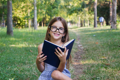Portrait of cute girl reading book while sitting at park