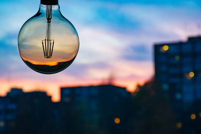 Close-up of illuminated lights against buildings in city at sunset