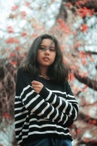 Portrait of beautiful young woman standing against trees