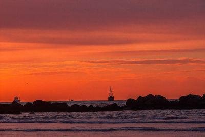 Silhouette sailboats on sea against orange sky