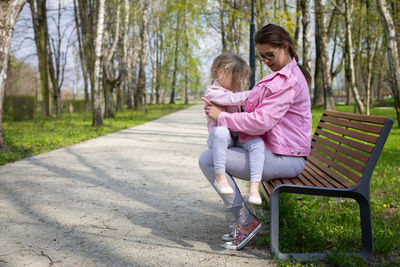 A girl looks at her mother behind her jacket. resting in the park on a bench.