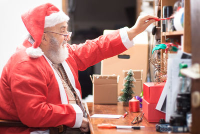 Side view of senior man in santa claus costume sitting at home