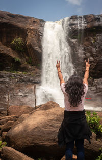 Girl solo traveler at waterfall with cloudy sky and green forests of the western ghat range