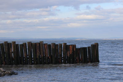 Wooden posts in sea against cloudy sky
