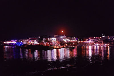 Reflection of illuminated buildings in lake against sky at night