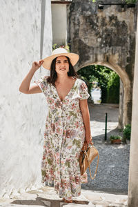 Front view of young woman wearing sundress, walking in street of old town