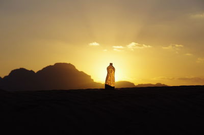 Silhouette person standing on land against sky during sunset