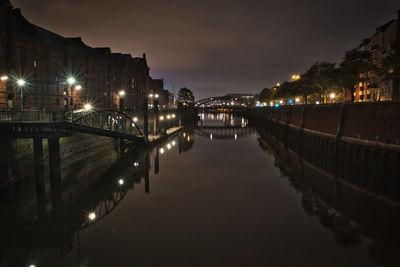 Illuminated bridge over river in city at night