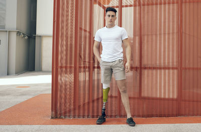 Confident disabled man with hand in pocket standing against orange wall