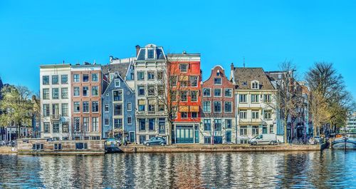 Buildings by river against clear blue sky traditional amsterdam architecture 