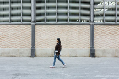 Woman walking on sidewalk by building while looking away