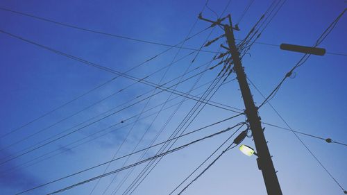 Low angle view of electricity pylon against blue sky