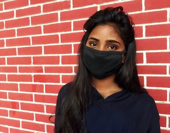 Portrait of young woman against brick wall wearing black mask 