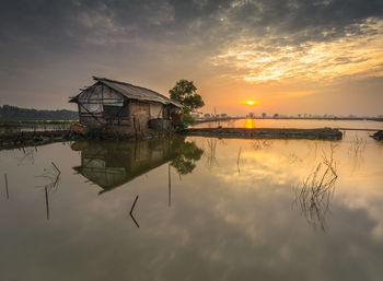 House by lake against sky during sunset