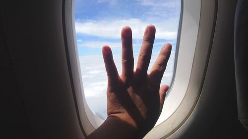 Cropped hand touching window in airplane