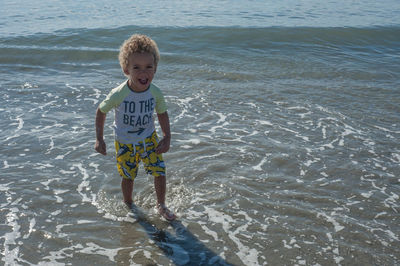 Playful boy standing in shallow water at beach