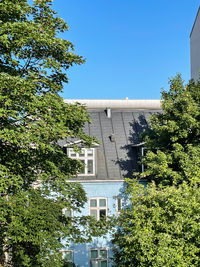 Low angle view of trees and buildings against clear blue sky