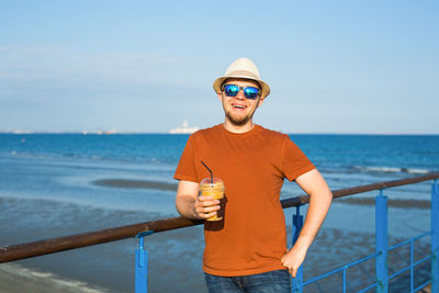 Portrait of man wearing sunglasses standing by railing against sea
