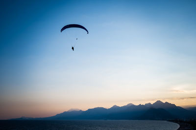 Low angle view of person paragliding against sky during sunset