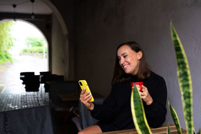 Young woman alone drinking in cafe on the terrace with a smartphone in her hands