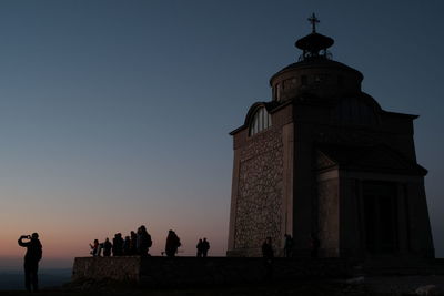 Group of people at mosque against clear sky during sunset
