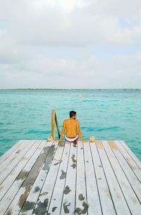 Rear view of woman sitting on jetty against sea