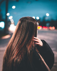 Rear view of woman standing on illuminated street at night