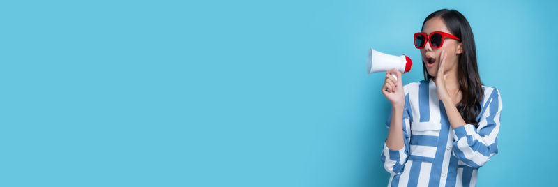 Woman holding umbrella standing against blue wall