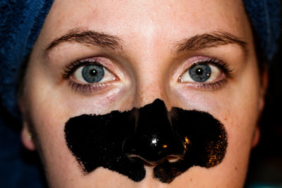 Close-up portrait of young woman with black facial mask on nose