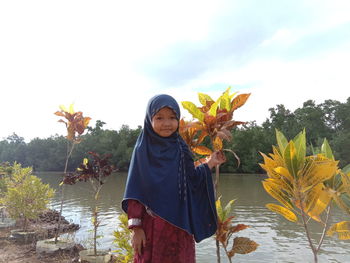 Portrait of girl in hijab standing by plants against lake