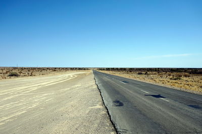 Tire tracks on road against clear blue sky