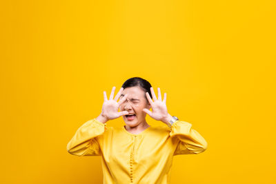 Woman showing stop gesture while standing against yellow background