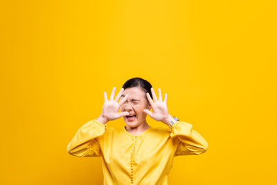 Portrait of smiling young woman against yellow background