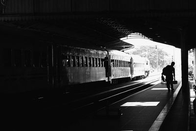 Silhouette man walking with luggage at railroad platform