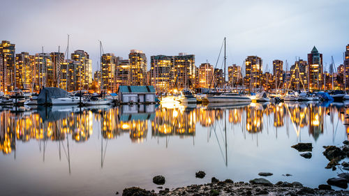 Sailboats moored in harbor by buildings against sky