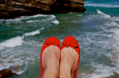 Low section of woman in red shoes against river