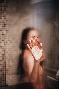 Naked woman taking shower seen through glass in bathroom