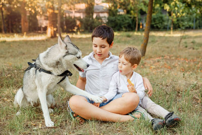 Brothers looking at dog while sitting on grass outdoors