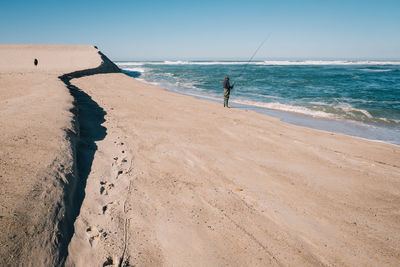 Man fishing at beach against clear sky