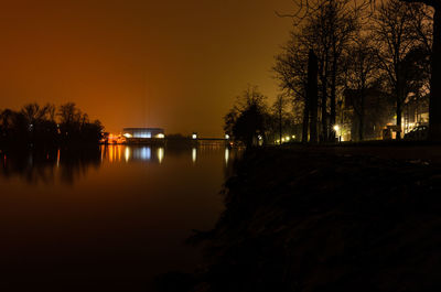 Silhouette trees by lake against sky at night