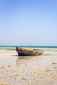 Boat moored on beach against clear sky