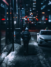 Rear view of man standing on snow covered street at night