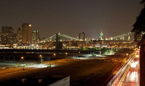 Illuminated bridge over river by buildings against sky at night